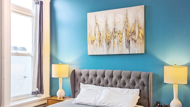 Ein Schlafzimmer mit einem Bett, zwei Nachttischen, einem Fenster und einem Wandbild.