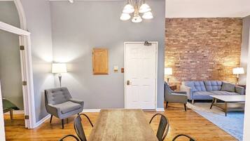 A dining area with a wooden table and chairs, a gray sofa, and a brick wall.