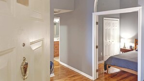 A room with a wooden floor, a bed with a striped blanket, a nightstand with a lamp, and a door with the number 3. - Tanner Bldg Apt 3 - 2 bedroom (Downtown) (Bay City)