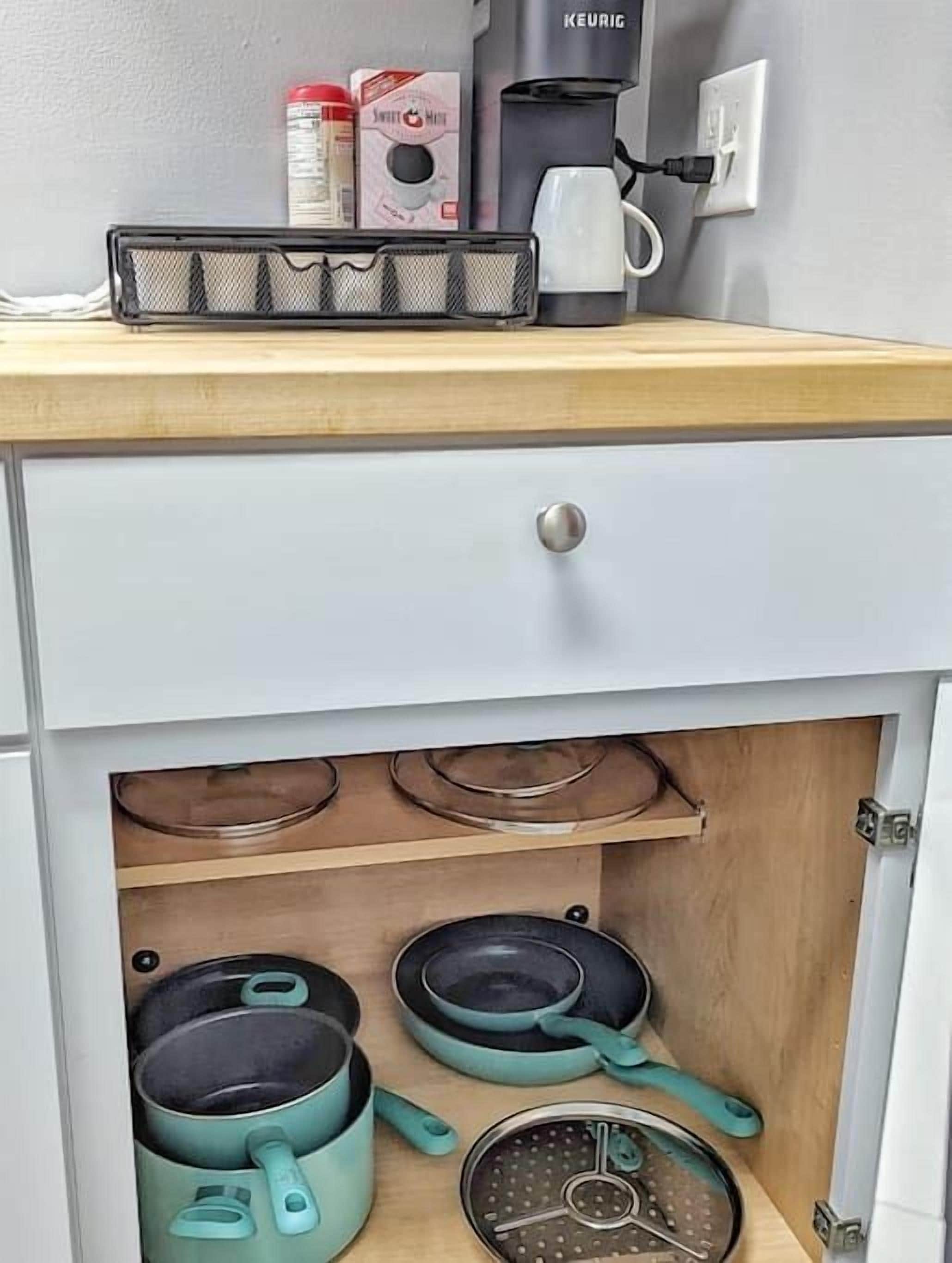 Ett kök med en kaffebryggare, en kaffekanna och en espressomaskin på bänkskivan. Tre kastruller och stekpannor förvaras i ett skåp under bänkskivan.