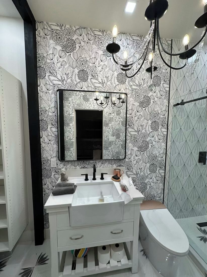 A bathroom with a white sink, mirror, and toilet. There is a chandelier above the sink.