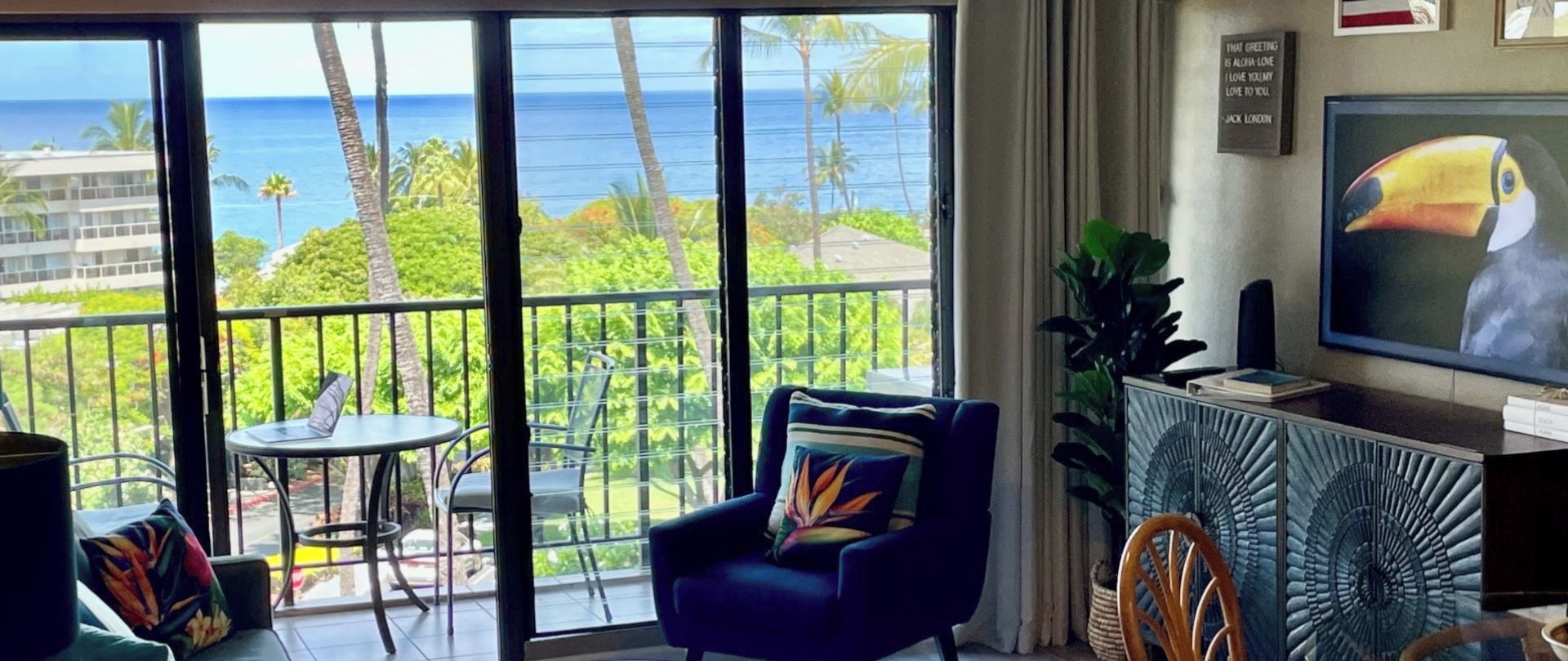 Ein Wohnzimmer mit einem großen Fenster und Blick auf den Ozean, einem Sofa, einem Sessel, einem kleinen Tisch und einem Fernseher.