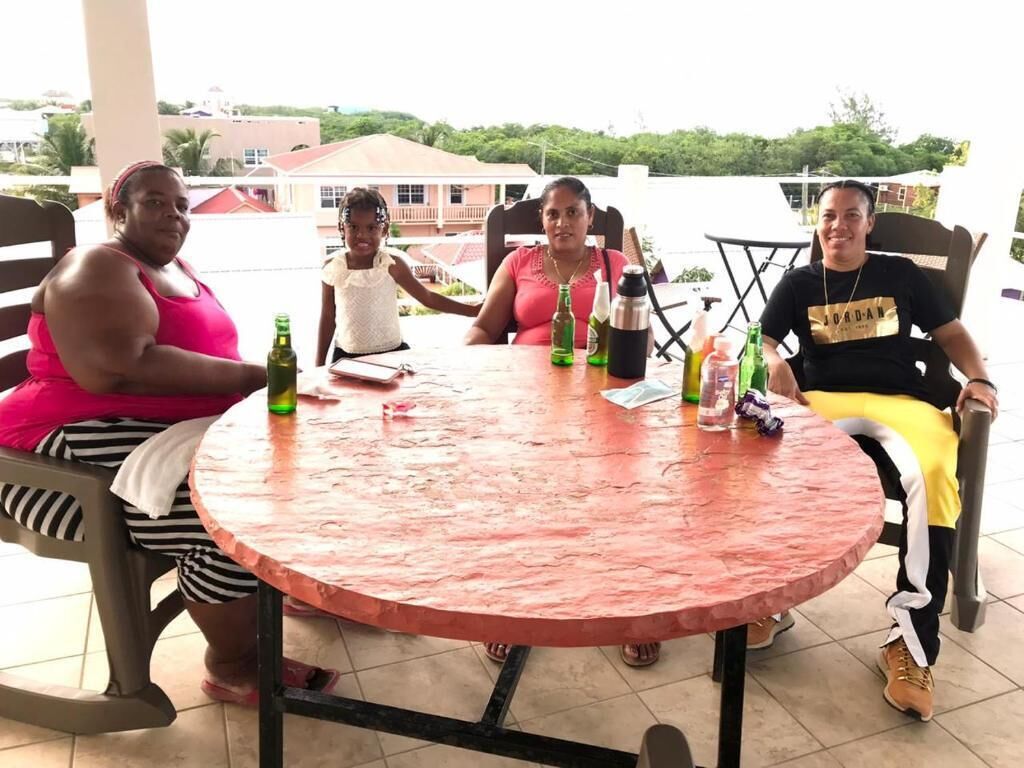 Un groupe de personnes est assis autour d’une table ronde recouverte d’une nappe rouge. On y voit également diverses bouteilles et un carnet.