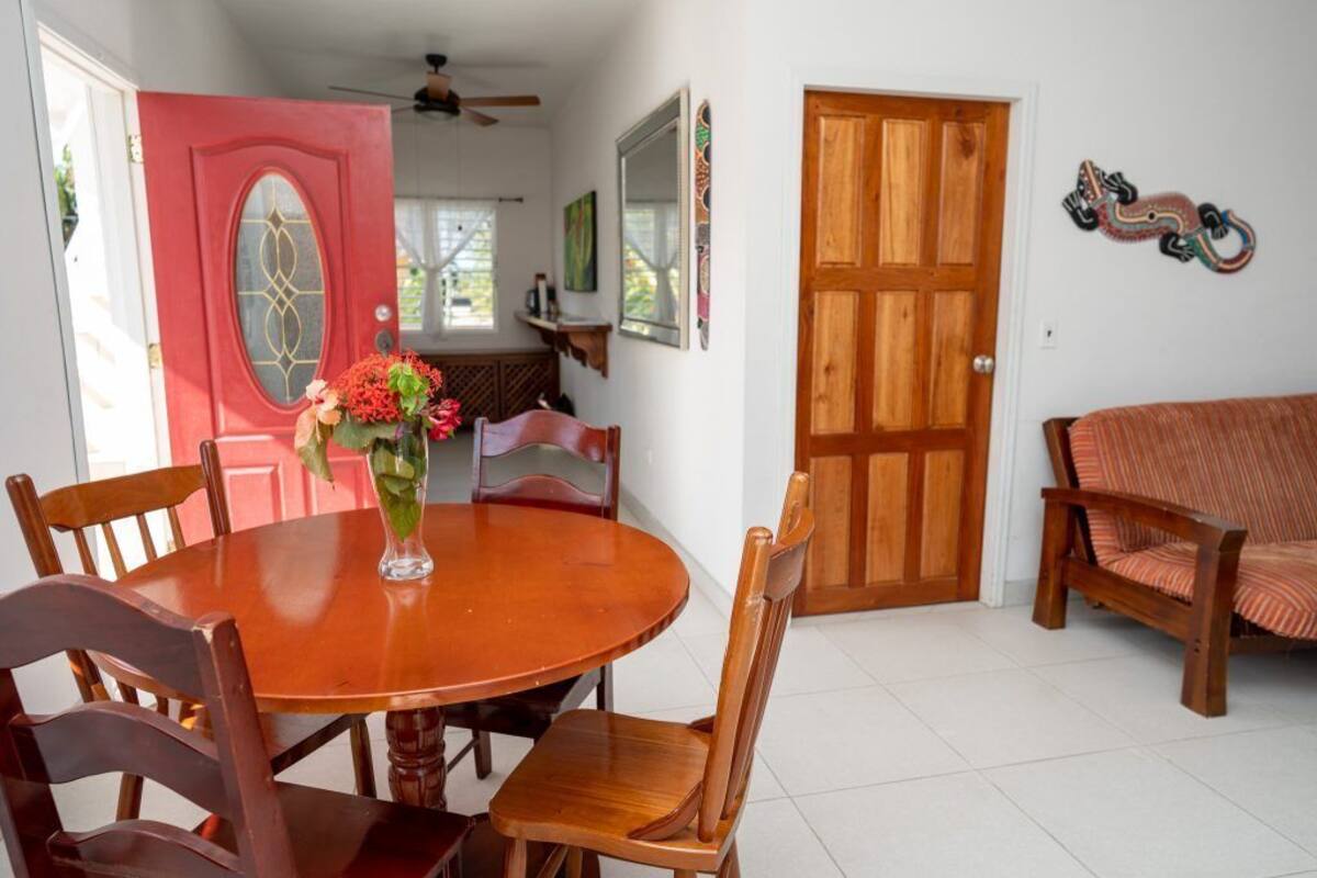 A dining area with a wooden table and chairs, a vase with flowers, a red door, and a wooden door.