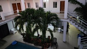 A multi-level building with a central courtyard featuring a pool and palm trees. There are multiple balconies and a staircase. - Seremei Villas (Caye Caulker)
