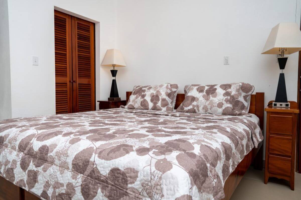 A bedroom with a large bed, two bedside tables, a wooden wardrobe, and two wall-mounted lamps.