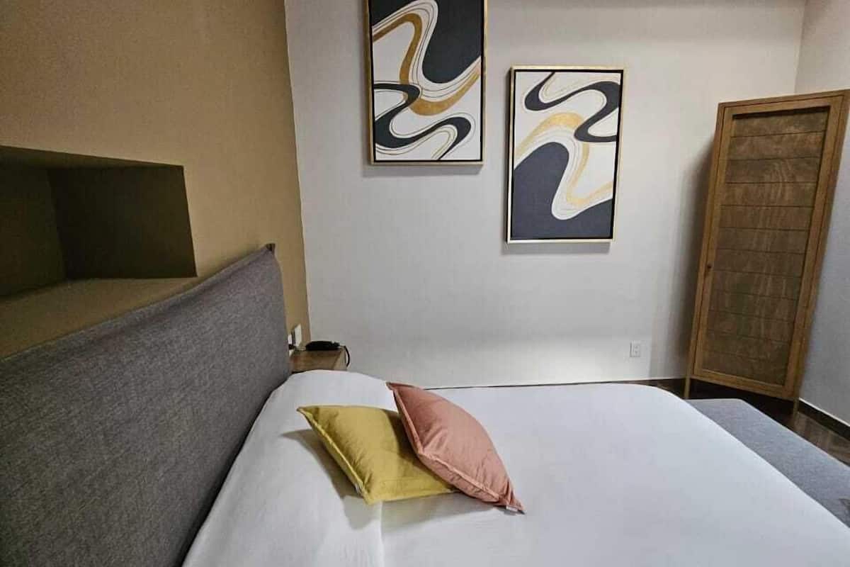 A bedroom with a bed, two pillows, a headboard, and two abstract paintings on the wall.