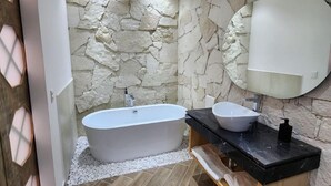 A modern bathroom with a freestanding bathtub, a round mirror, and a black marble countertop. - Hotel Úrsula Concept (Querétaro)