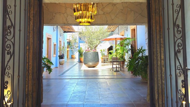 An entrance with a stone floor, a large chandelier, and a view of the courtyard with potted plants and outdoor seating. - Hotel Úrsula Concept (Querétaro)