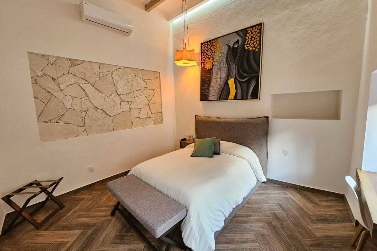 A bedroom with a bed, a bench, a wall art piece, and a hanging light fixture.