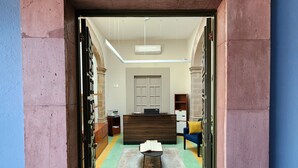 A reception area with a reception desk, a bench, and a door leading to a hallway. - Hotel Úrsula Concept (Querétaro)