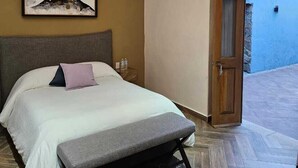 A bedroom with a bed, a bench, a painting, and a view of the outside. - Hotel Úrsula Concept (Querétaro)