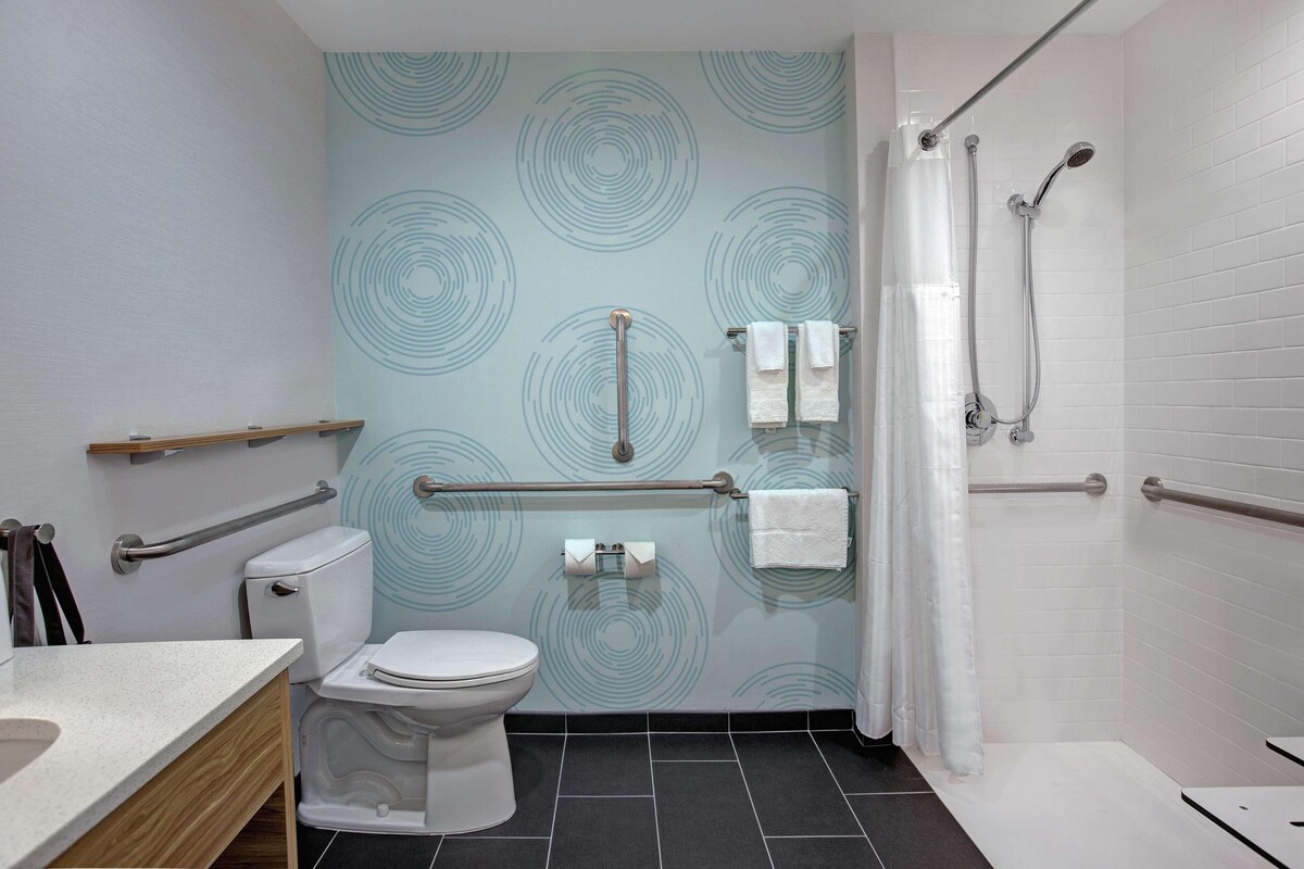 A modern bathroom with a toilet, bidet, and shower. It features a patterned wall, grab bars, and a towel rack.