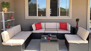 Ein überdachter Patio-Bereich mit einer Eckcouch, zwei Beistelltischen und Topfpflanzen.