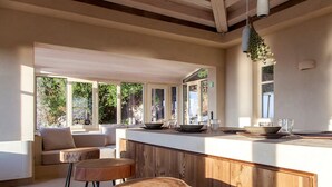 A modern kitchen with a wooden island, bar stools, and large windows offering views of greenery. - Villa Dalula in Agios Nikitas (Lefkada)