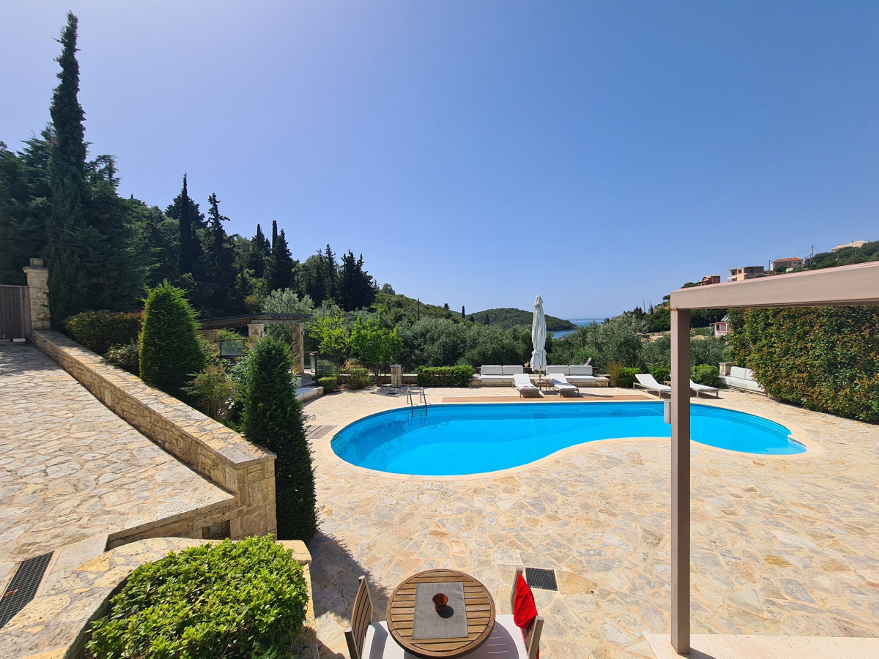 Une piscine entourée de murs de pierre et de verdure, avec des chaises longues et une table à proximité.