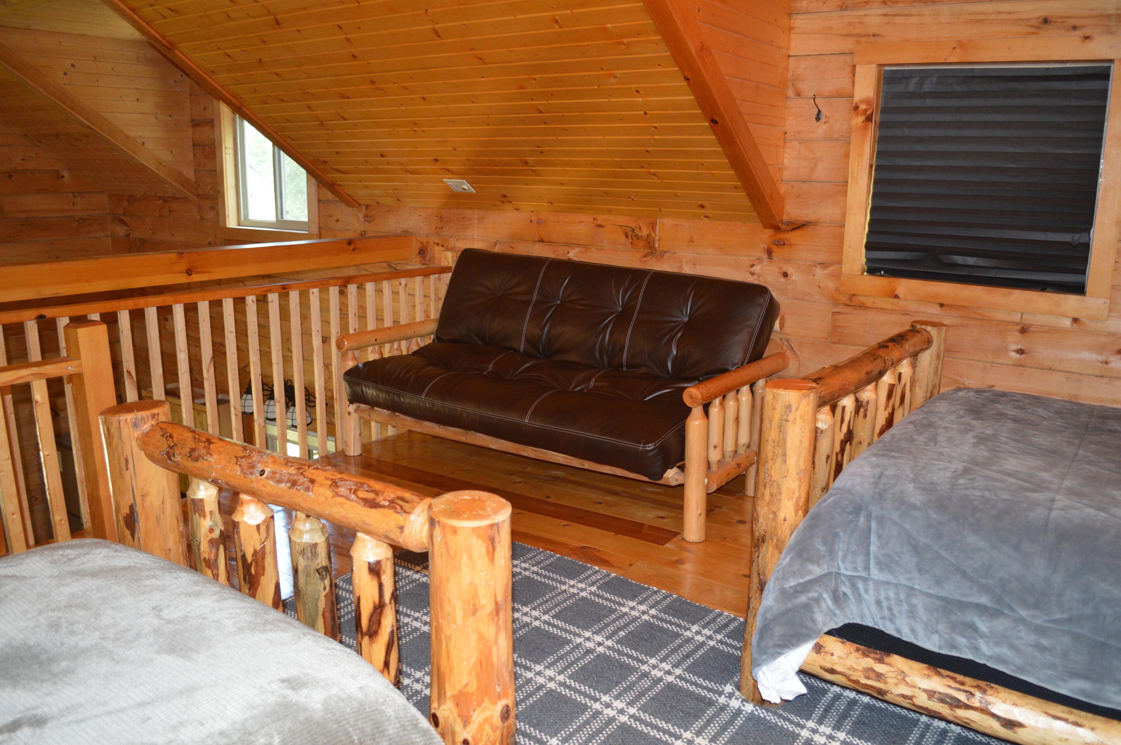 A cabin interior with a wooden ceiling, a sofa, a bed, and a window.