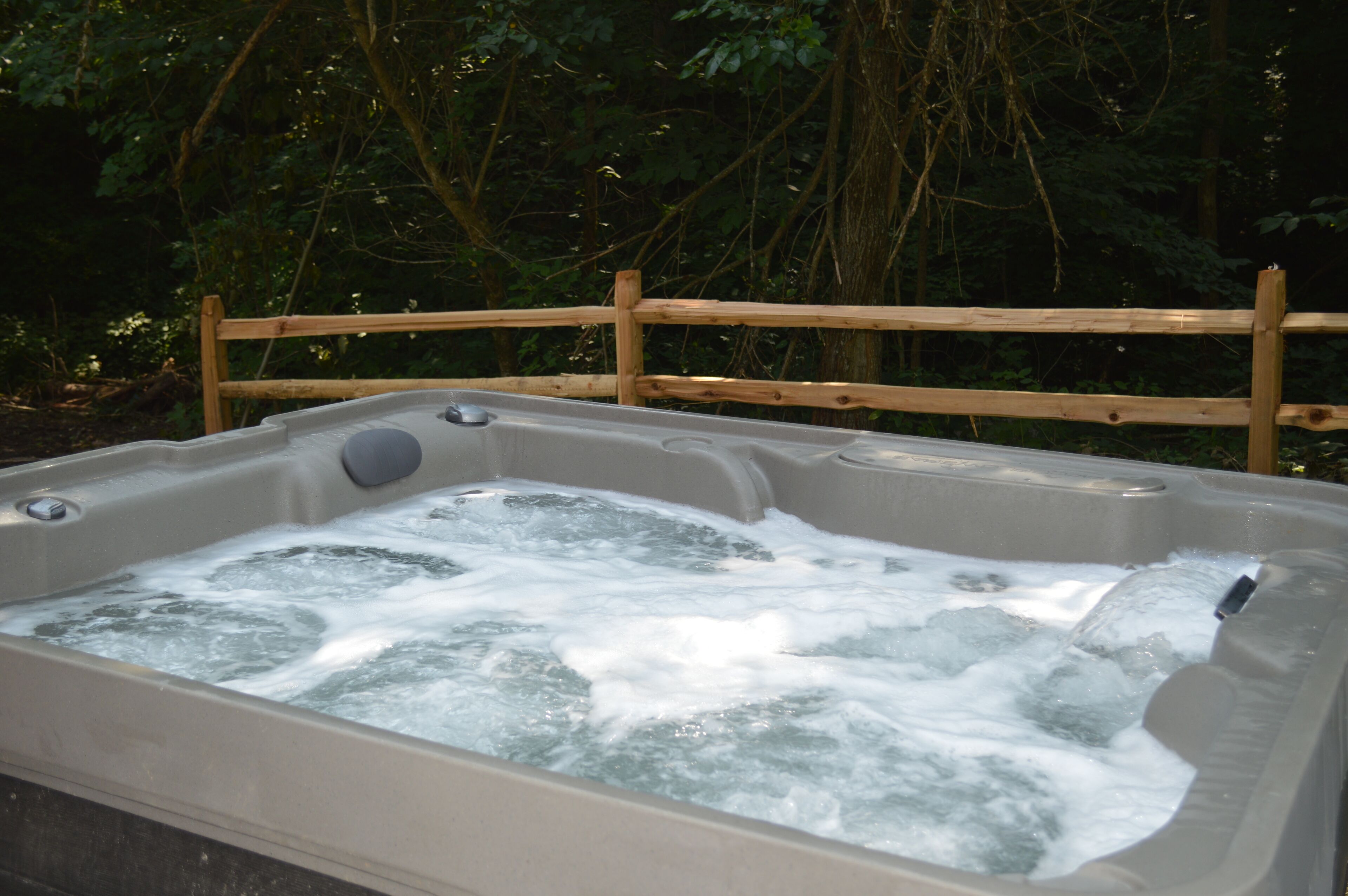 Un bain à remous entouré d’une clôture en bois, situé dans un endroit boisé.