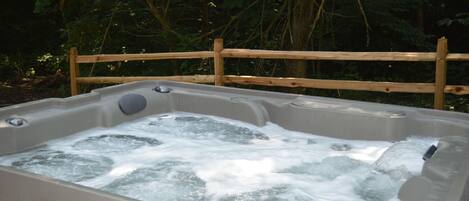 Un bain à remous entouré d’une clôture en bois, situé dans un endroit boisé.