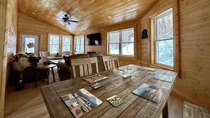 A cozy cabin interior with a wooden ceiling, a dining table with placemats, leather sofas, and a television mounted on the wall. - Cozy Secluded Cabin w/ Hot Tub, Relax, Unwind & Stargaze (Ferryville)
