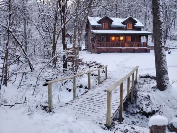 A wooden cabin with a porch and a wooden bridge leading to it, surrounded by snow-covered trees. - Cozy Secluded Cabin w/ Hot Tub, Relax, Unwind & Stargaze (Ferryville)