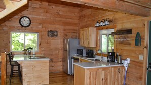 A wooden cabin kitchen with a central island, a refrigerator, microwave, and a sink. - Cozy Secluded Cabin w/ Hot Tub, Relax, Unwind & Stargaze (Ferryville)