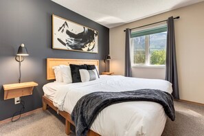 Un dormitorio con cama, mesitas de noche, una lámpara de pared, una ventana con cortinas y un cuadro en la pared.