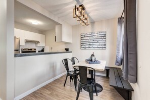 Una cocina compacta con zona de comedor, que presenta una lámpara moderna, suelo de madera y un diseño minimalista.