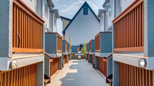 A row of modern, single-story homes with wooden fences and a central pathway leading to a blue-roofed building.