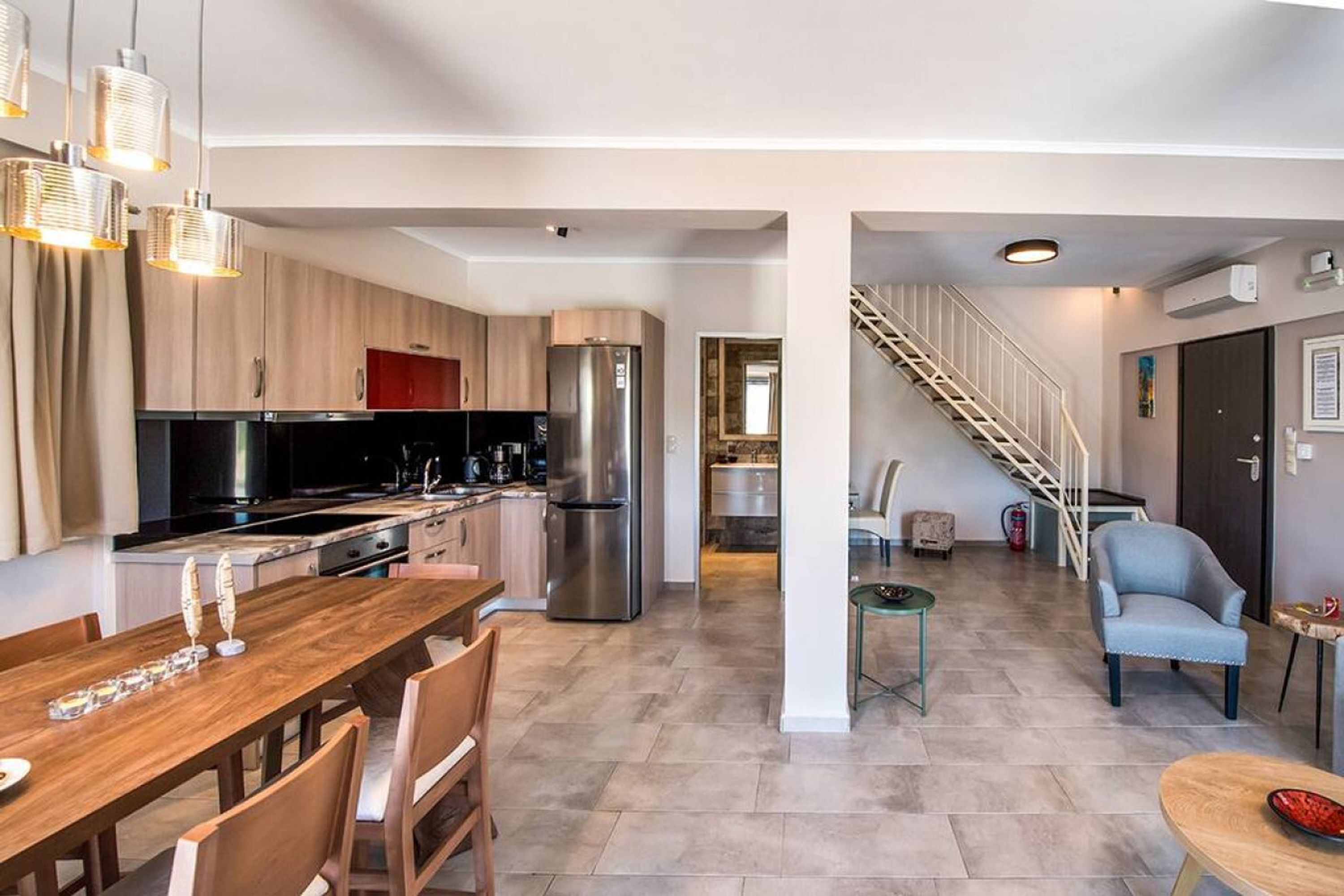 A modern kitchen with stainless steel appliances, a wooden dining table, and a staircase leading to an upper level.