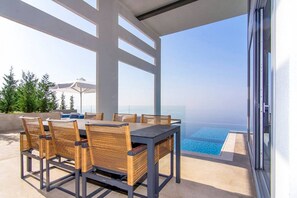 Un área de comedor al aire libre con vista al océano, una piscina y un espacio de estar cubierto con sombrillas.