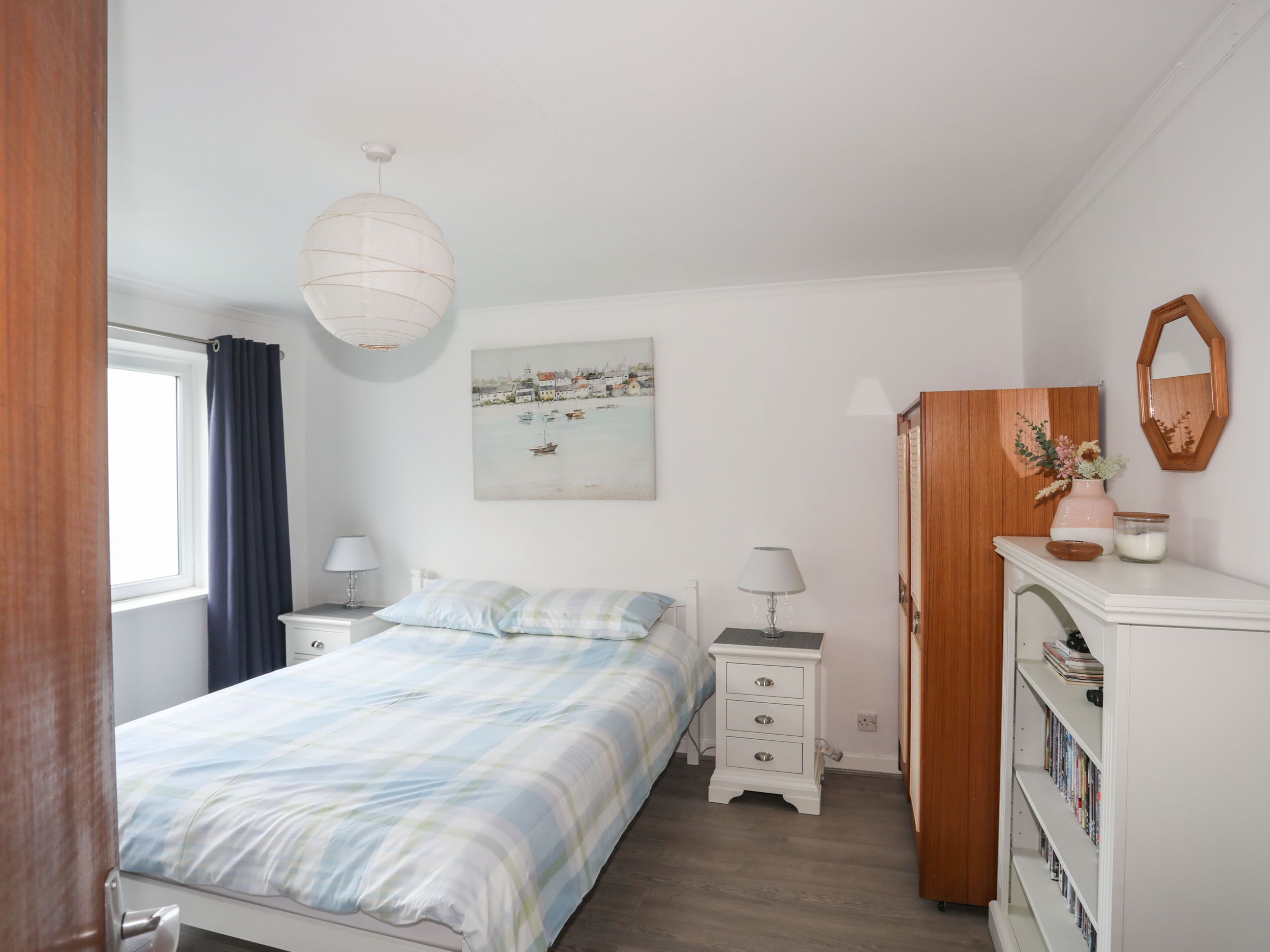 Une chambre à coucher comprenant un lit, des tables de chevet, une commode, un meuble à tiroirs, un miroir et une fenêtre avec des rideaux.