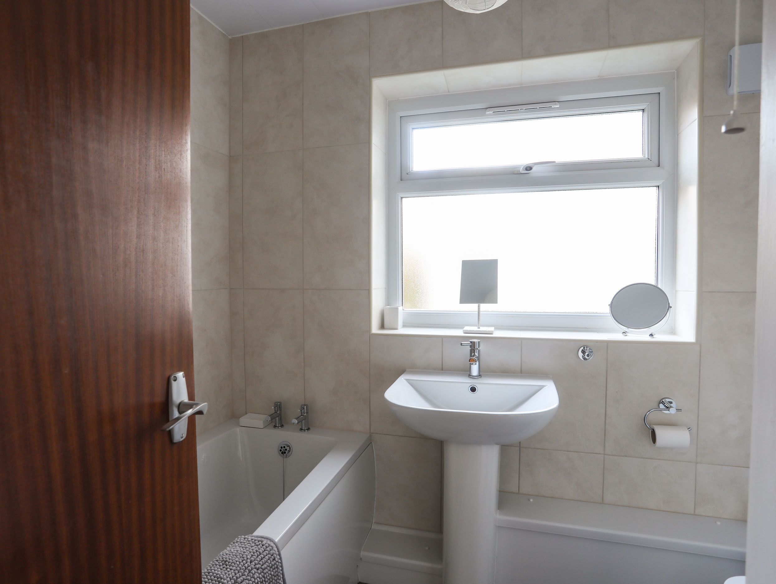 A bathroom with a bathtub, a sink, a window, and a mirror.
