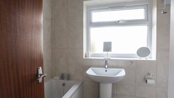 A bathroom with a bathtub, a sink, a window, and a mirror.