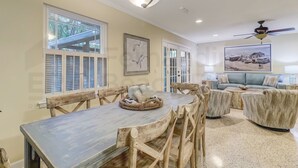 A spacious dining area with a wooden table and chairs, a large window with shutters, and a ceiling fan. - 223 Lighthouse Circle 3 Bedroom Home by RedAwning (Fernandina Beach)