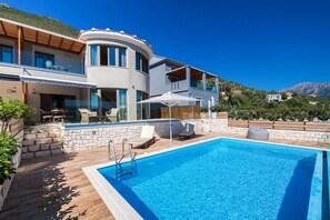 Eine moderne Villa mit Swimmingpool, Steinmauern und Blick auf die umliegenden Hügel.