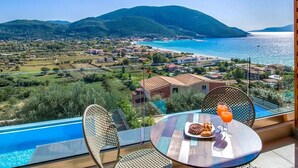 A balcony with a view of a coastal town, a swimming pool, and a table with food and drink. - Villa Mare 3 Aria Drakatos (Lefkada)