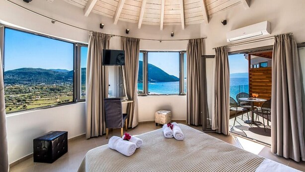 A hotel room with a large bed, a TV, a small table with drinks, and a balcony with a view of the sea and mountains. - Villa Mare 3 Aria Drakatos (Lefkada)