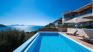 A modern pool with clear blue water, surrounded by a stone deck and lounge chairs, overlooking a scenic view of the sea and distant mountains. - Villa Mare 3 Aria Drakatos (Lefkada)