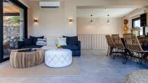 Ein modernes Wohnzimmer mit einer Couch, einem Hocker und einem Essbereich mit Stühlen.