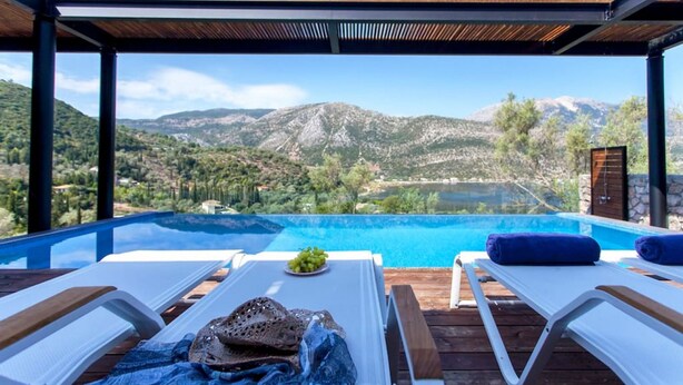 Ein Infinity-Pool mit Blick auf die Berge, zwei Liegestühle und ein Tisch mit einer Flasche und Trauben.