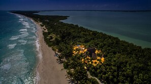 An aerial view of a beach with a small resort area featuring a few buildings and palm trees. - Casa Nalum (Tulum)