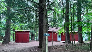 A red cabin with a door and a window, surrounded by trees. - Waterfront Pine Cabin near Saratoga, Lake George (Corinth)