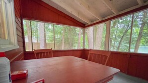 A wooden dining room with a large table and benches, large windows with a view of trees, and a red patterned rug on the floor. - Waterfront Pine Cabin near Saratoga, Lake George (Corinth)
