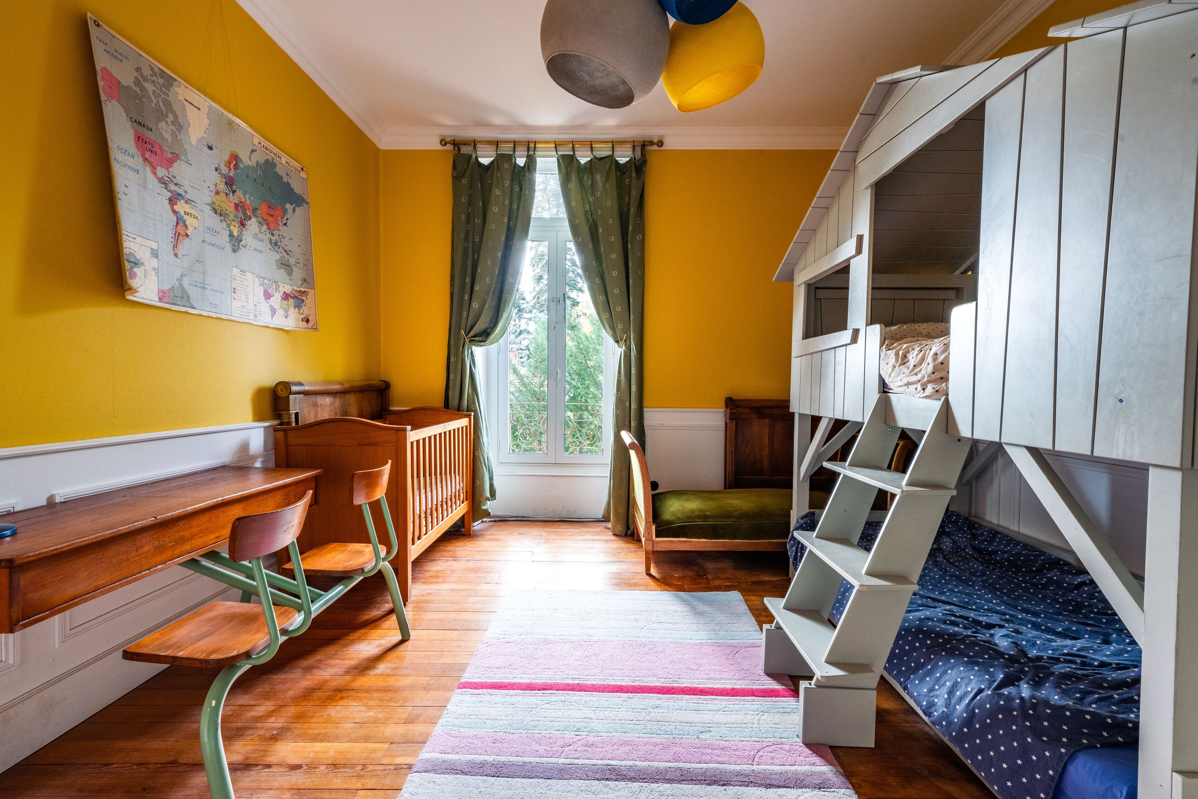 A room with a wooden desk, a green chair, a bunk bed, and a window with curtains.