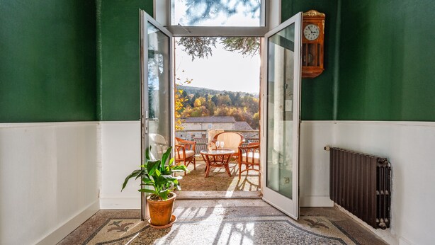Ein Zimmer mit Blick auf eine Terrasse, einem Blumentopf und einer Holzuhren an der Wand.