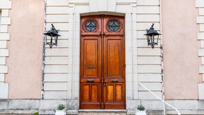 Eine hölzerne Doppeltür mit je einem Laternenpaar an den Seiten, eingebaut in ein Gebäude mit Steinunterbau und weißem Außenputz.