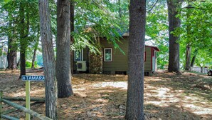 Un chalet rustique entouré de grands arbres, avec un sol en terre battue et une enseigne en bois indiquant le nom « TAMARA ».