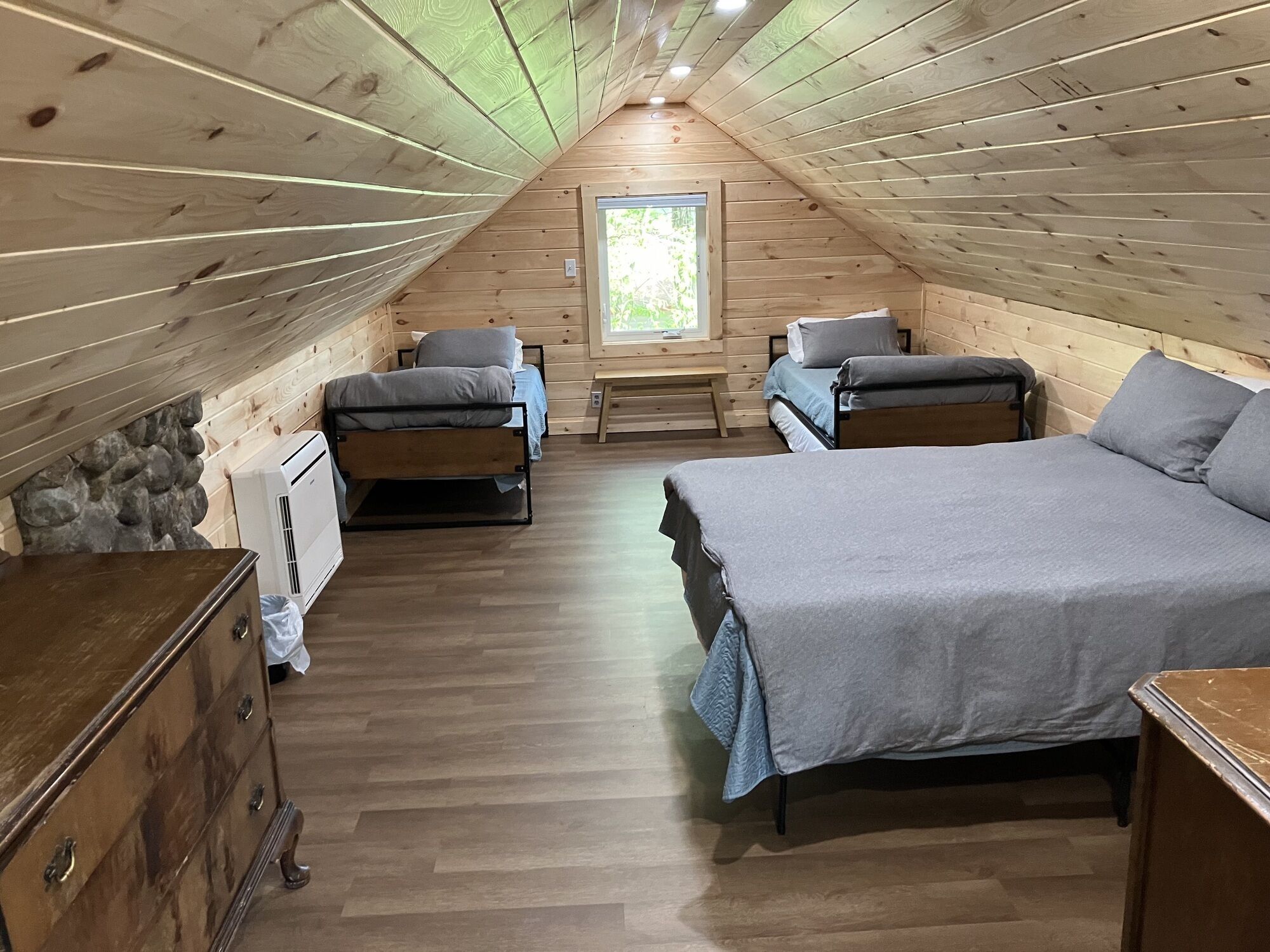 Une chambre confortable située sous les toits, avec deux lits, un mur en pierre et une fenêtre.