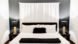 A neatly made bed with white bedding, a black throw, and a black pillow. There are two bedside tables with lamps and decorative vases.